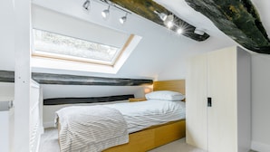 Un dormitorio con tragaluz, una cama con colcha blanca, cabecera de madera y un armario.