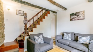 Una sala de estar con una escalera, dos sofás grises con cojines estampados, una mesa de centro de madera y un cuadro enmarcado en la pared.