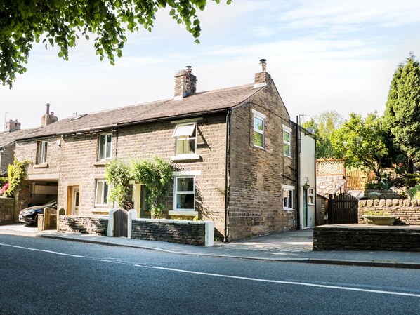 A two-story stone house with a garage, a small garden, and a paved driveway. - Rose Cottage (High Peak)