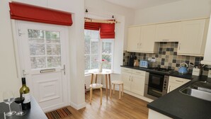 A kitchen with a dining area, wooden flooring, and a view of greenery outside. - Cherry Tree Cottage (Skipton)