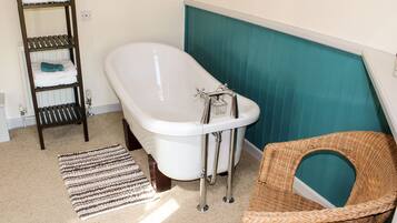 Une salle de bain avec une baignoire blanche, une chaise en osier, un tapis à rayures et une échelle en bois.