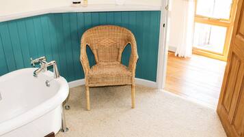 A bathroom with a white bathtub, a wicker chair, teal walls, and a wooden door.