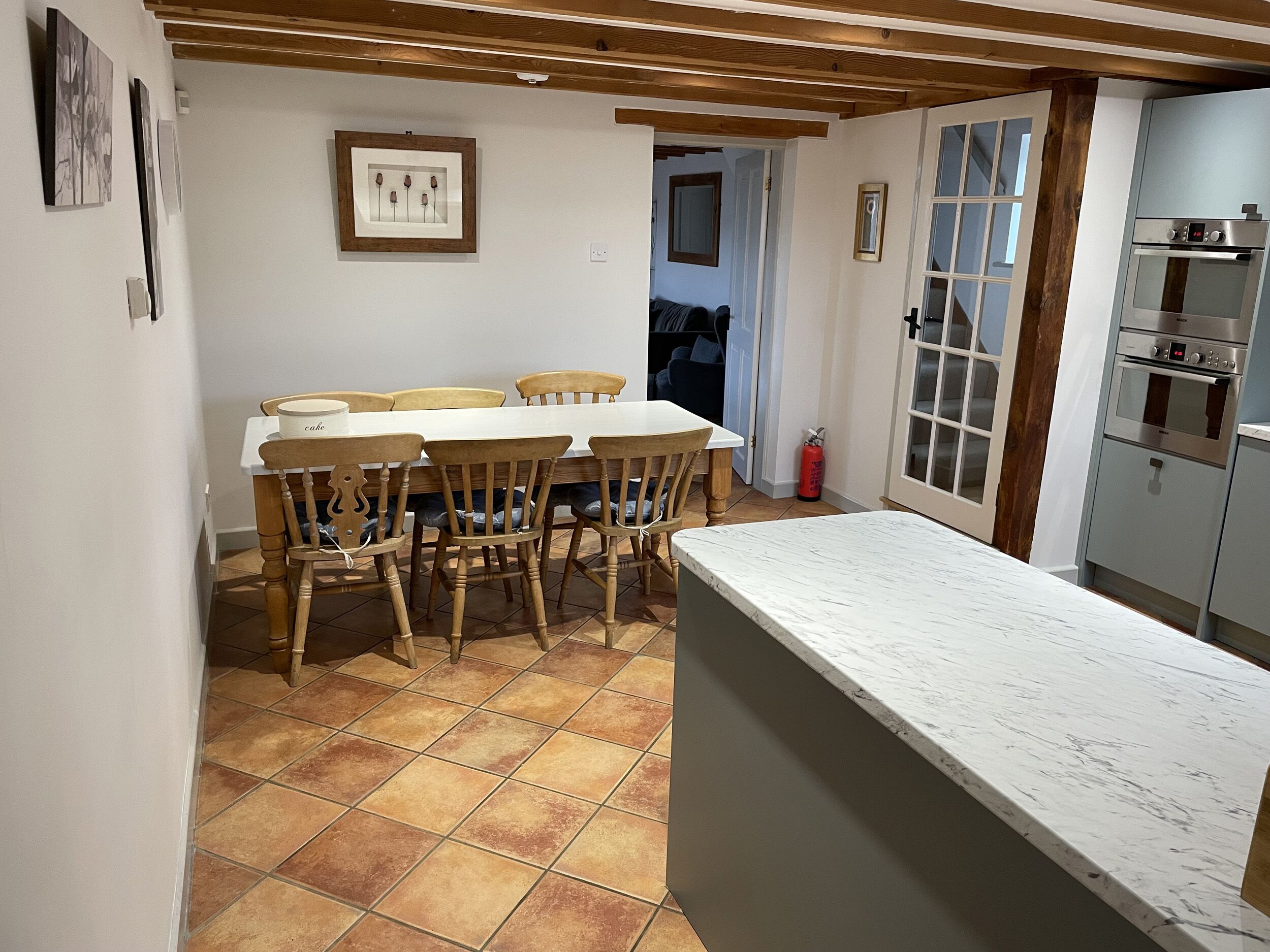 Une cuisine avec un plan de travail en marbre blanc, des chaises en bois et un sol carrelé.