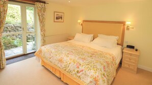 A bedroom with a bed, a nightstand, a lamp, a picture on the wall, and a window with curtains.