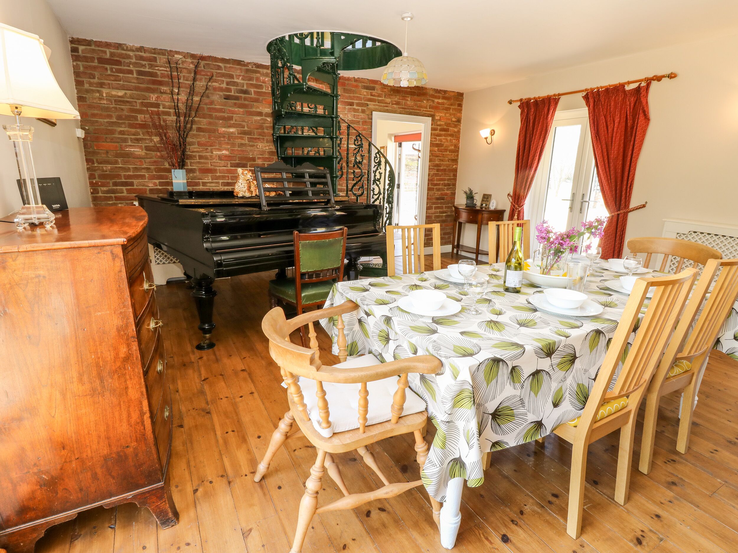 Un coin repas avec un piano, des chaises en bois, une table dressée pour quatre personnes et un mur en briques.