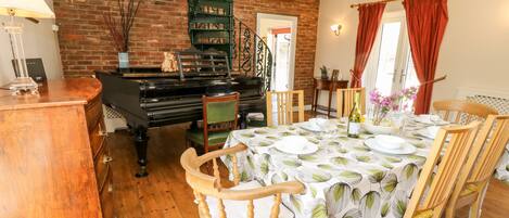Un coin repas avec un piano, des chaises en bois, une table dressée pour quatre personnes et un mur en briques.