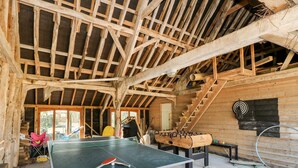 Une pièce rustique en bois, avec une table de ping-pong, un baby-foot et un escalier.