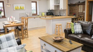 A modern kitchen with white cabinets, a central island, and wooden stools. - Woodman's Lodge (Nantwich)