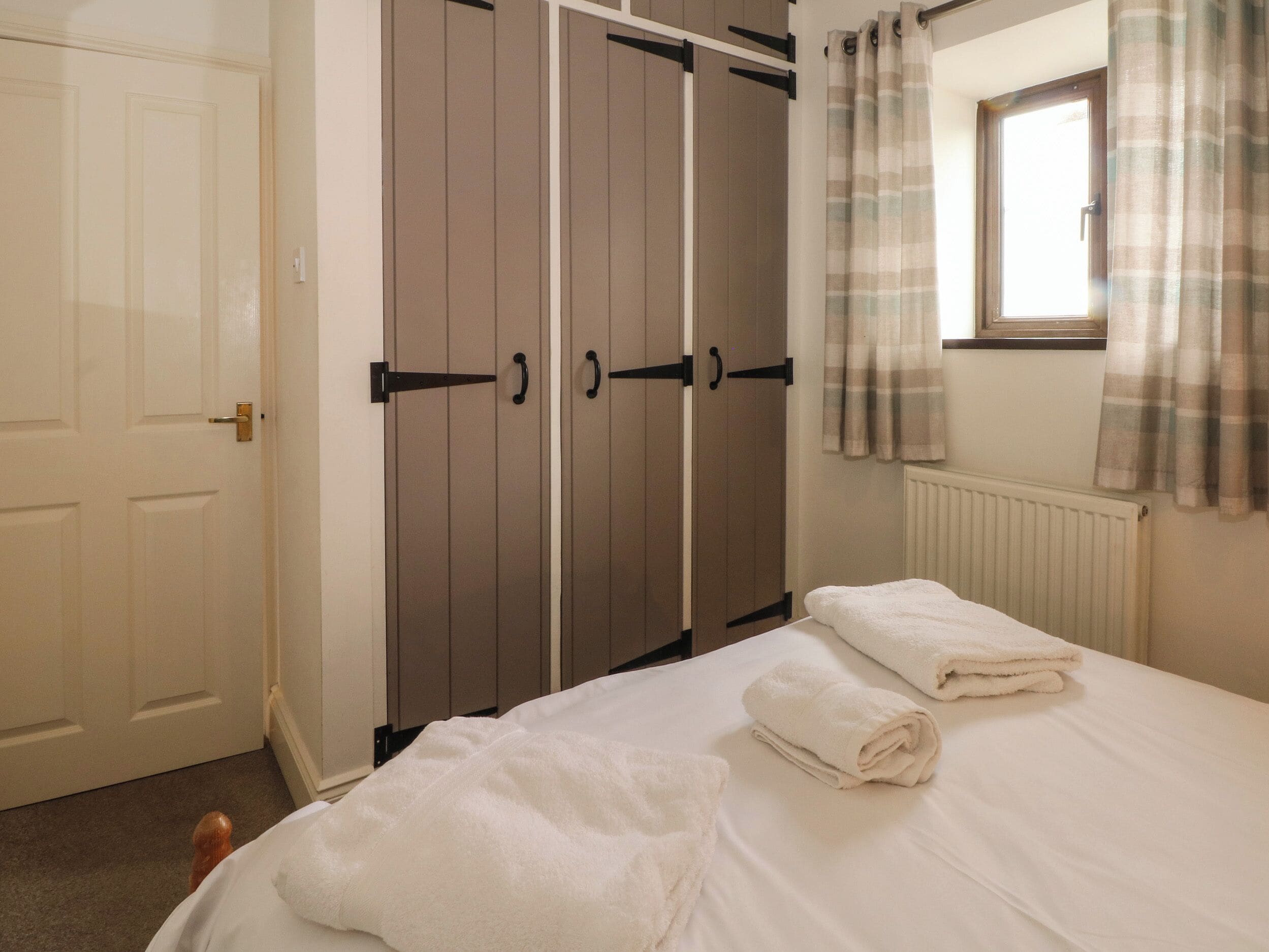A bedroom with a bed, two towels, a wardrobe, and a window with curtains.