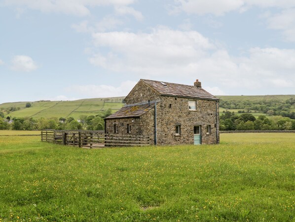 A stone farmhouse with a wooden fence in a grassy field.
