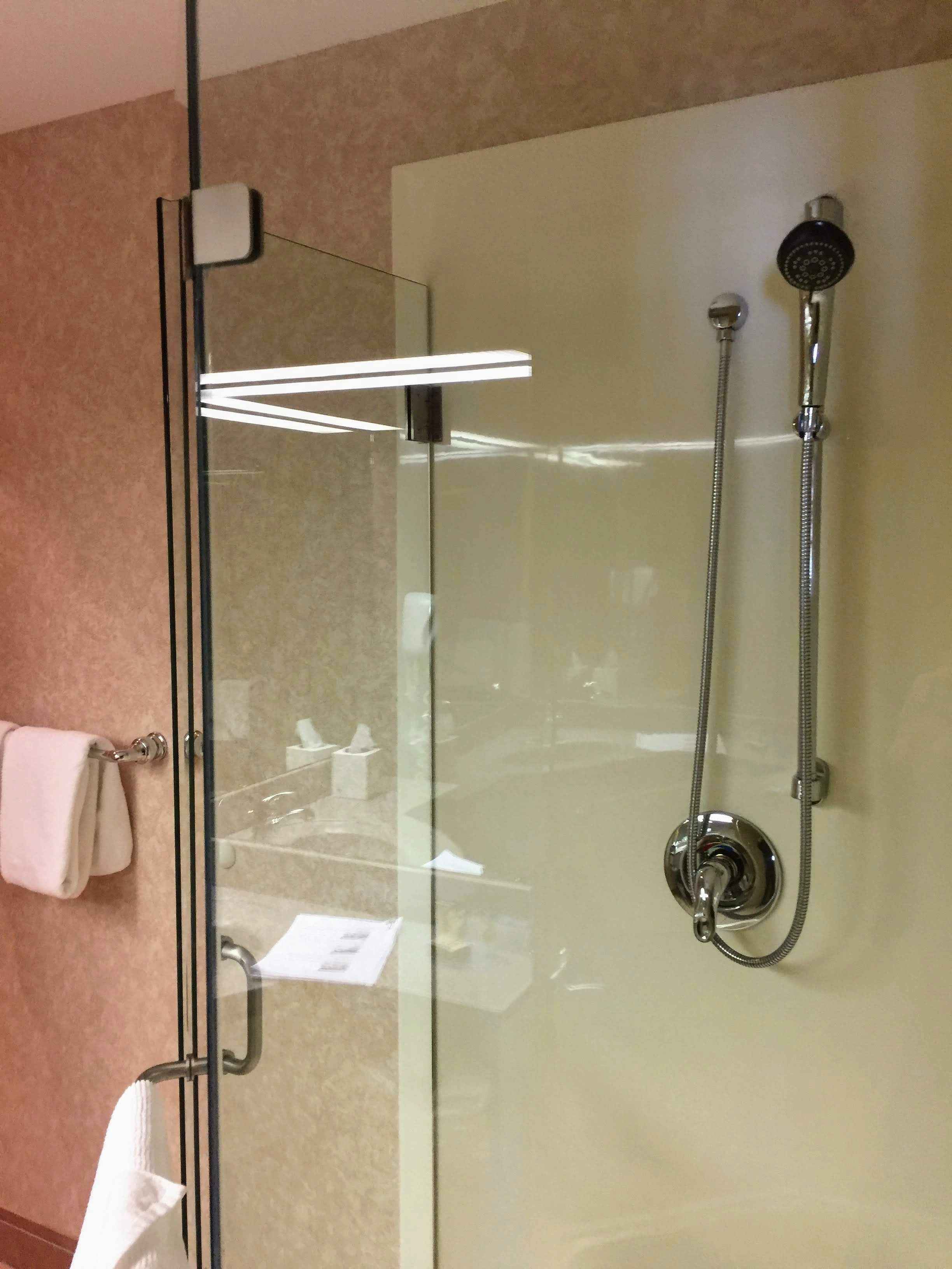 A glass-enclosed shower with a handheld showerhead and a wall-mounted faucet.