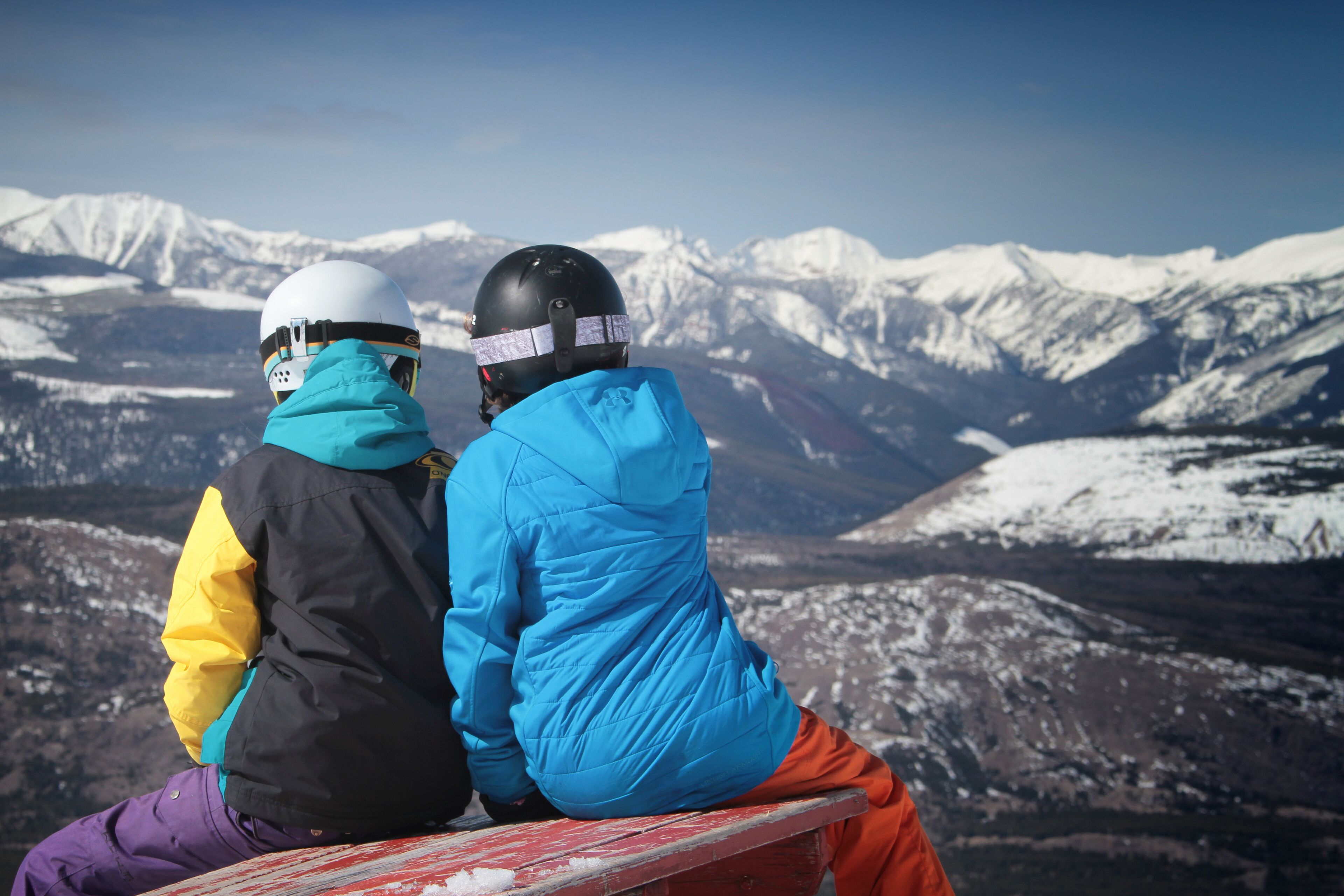 Two people sitting on a bench with a snowy mountain landscape in the background.
