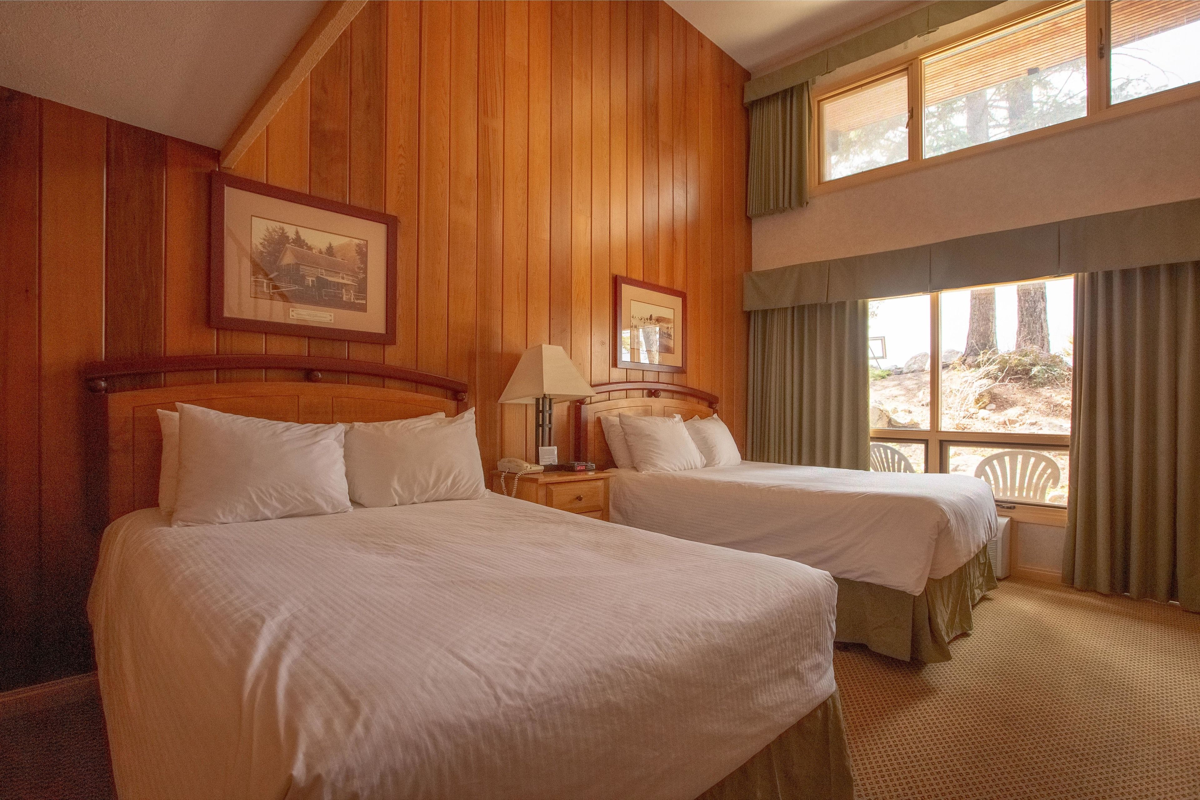Une chambre avec deux lits, des lambris en bois, des tableaux encadrés au mur et une fenêtre avec des rideaux.