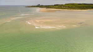 A coastal landscape with a sandy beach, calm waters, and a distant hill with a structure. - Bay View (Belford)