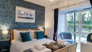 A bedroom with a large bed, a bedside table, a chair, and a window with a view of greenery. - Bay View (Belford)