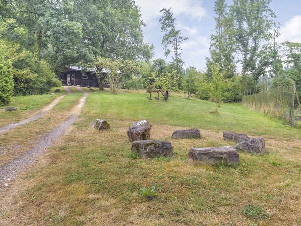 Ländliche Landschaft mit einem Kiesweg, der zu einer Holzhütte inmitten von Bäumen und Felsen führt.