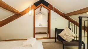A bedroom with a bed, a chair, a staircase, and a bathroom visible through an open door.