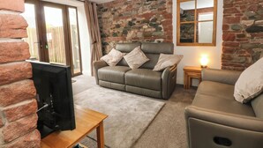 A cozy living room with a stone wall, a leather sofa, a wooden coffee table, and a television.