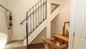A staircase with a wooden handrail and black balusters, leading to a landing with a wicker chair and a wooden desk.