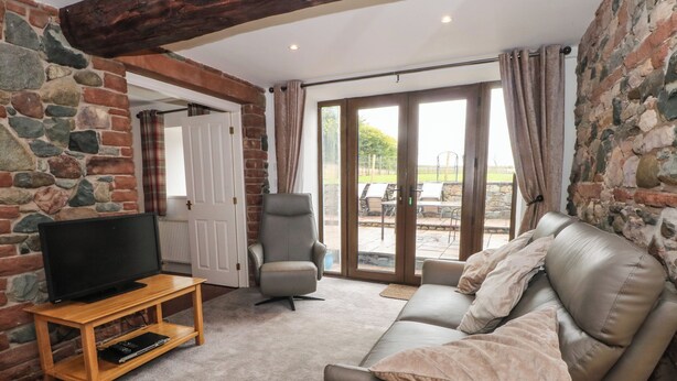 A living room with a stone wall, a sofa, a recliner, a TV on a wooden stand, and a sliding glass door leading to an outdoor area.