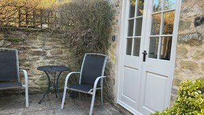 Un mur de pierre, une porte blanche et une petite terrasse avec deux chaises et une table.