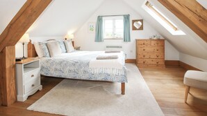 A bedroom with a sloped ceiling, a bed with a patterned bedspread, a dresser, a nightstand, and a window with curtains. - The Old Workshop (Shrewsbury)