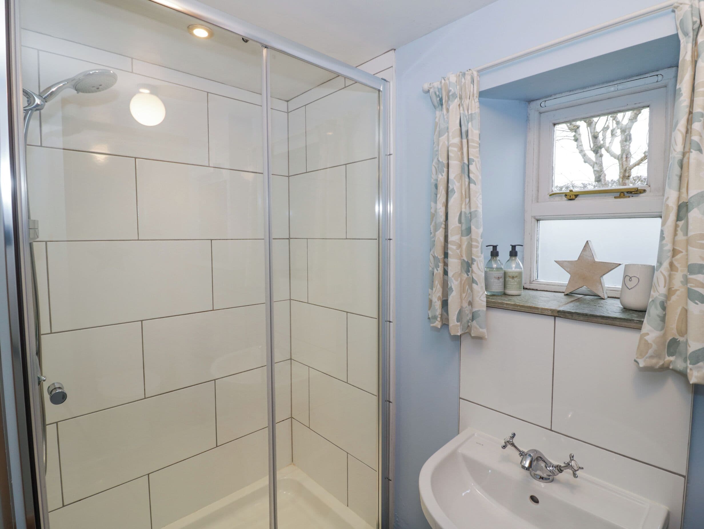 A bathroom with a glass-enclosed shower, a sink with a mirror above it, and a window with a star decoration.