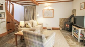 A cozy living room with a sofa, a plaid armchair, a television, a fireplace, and a wooden staircase. - The Old Workshop (Shrewsbury)