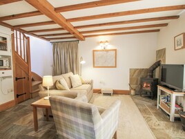 Una sala de estar acogedora con un sofá, un sillón a cuadros, un televisor, una chimenea y una escalera de madera.