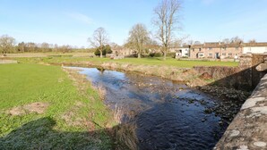 A rural landscape with a stream, grassy fields, and stone buildings. - Cherry Tree Cottage (Kirkby Stephen)