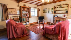 A cozy living room with wooden floors, a bookshelf, a television, and a desk with a lamp. - Cherry Tree Cottage (Kirkby Stephen)