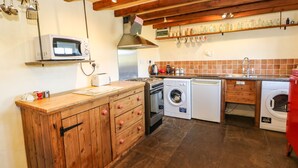 A kitchen with wooden cabinets, a microwave, a stove, a washing machine, and a sink. - Cherry Tree Cottage (Kirkby Stephen)