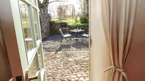 A stone patio with a table and chairs, a stone wall, and a tree. - Cherry Tree Cottage (Kirkby Stephen)
