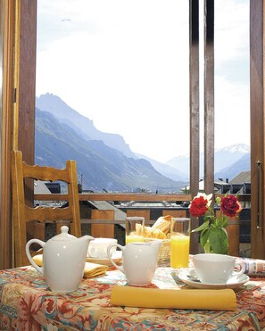 Desayuno con vistas a montañas, una silla de madera, una mesa con mantel floral y un jarrón con flores.