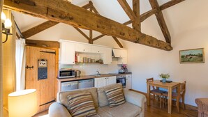 Un soggiorno accogliente con divano, tavolo da pranzo con sedie, angolo cottura con mobili e elettrodomestici bianchi, e travi a vista in legno al soffitto.