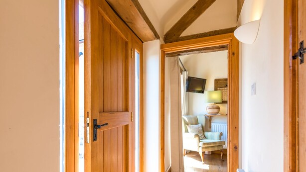 Una porta in legno che dà su una stanza con termosifone, televisore e lampada su uno scaffale.