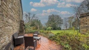 A patio with a brick floor and outdoor furniture, surrounded by stone walls and greenery.