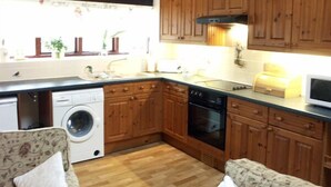 A compact kitchen with wooden cabinets, a washing machine, an oven, and a microwave. - Brook Cottage (Gillingham)