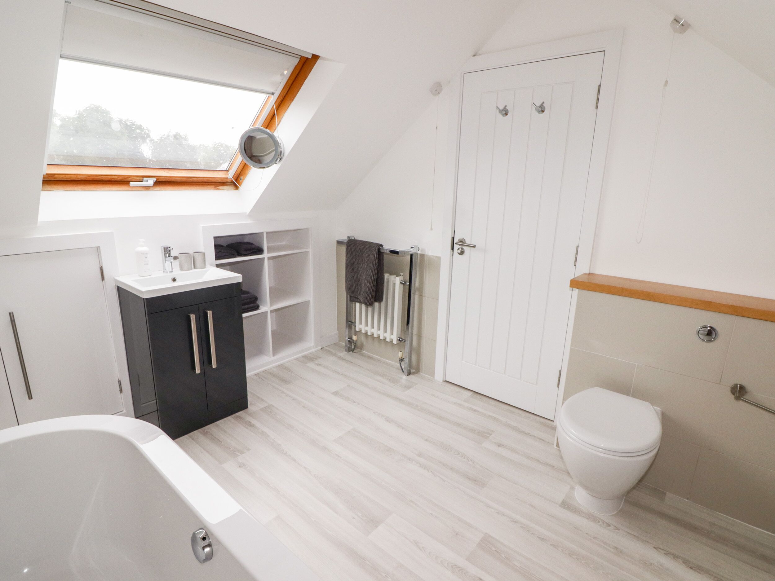 A modern bathroom with a skylight, a bathtub, a toilet, and a built-in shelf unit.