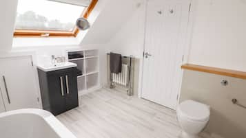 A modern bathroom with a skylight, a bathtub, a toilet, and a built-in shelf unit.