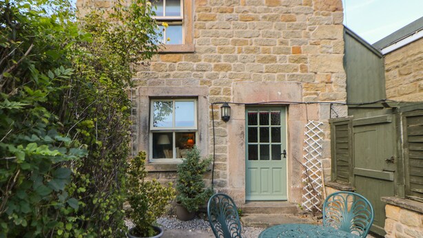 Une maison en pierre avec une porte verte, une fenêtre et un petit jardin agrémenté d’une table et de chaises.