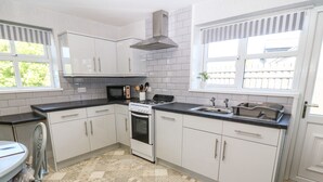 A modern kitchen with white cabinets, a gas stove, and a sink. - Beech Cottage (Tyn-y-Gongl)