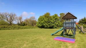 A playground with a slide and a climbing structure in a grassy area. - Beech Cottage (Tyn-y-Gongl)