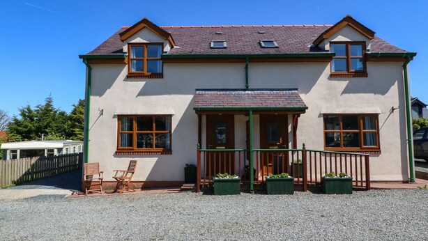 A two-story house with a gravel driveway, wooden bench, and potted plants. - Beech Cottage (Tyn-y-Gongl)