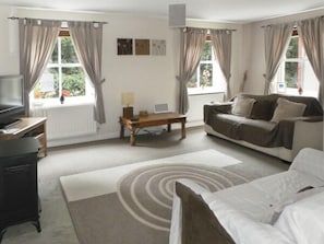 Relax in this inviting room with a sofa set, coffee table, and TV on a stand, plus a rug and two windows with a view.