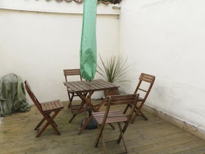 Relax in this serene patio area with a table and chairs under a shaded canopy, surrounded by lush greenery and a natural ambiance.