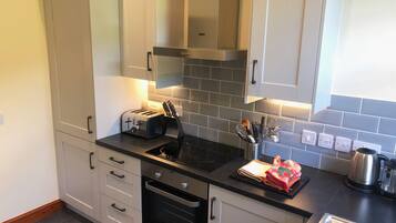 A modern kitchen with white cabinets, a black countertop, a built-in oven, and a stainless steel kettle.