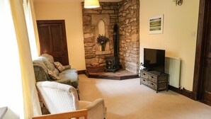 A cozy living room with a stone fireplace, a television, and a dining area with a table and chairs. - The Coach House (Duns)