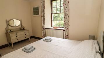 A bedroom with a bed, dresser, mirror, window with curtains, radiator, and a framed picture on the wall.