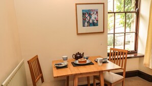 A dining table with chairs, a framed painting, and a window with a view of greenery. - The Coach House (Duns)